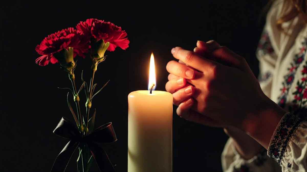 Запалена свіча пам'яті в руках жінки, чорна стрічка, червоні гвоздики, темний фон